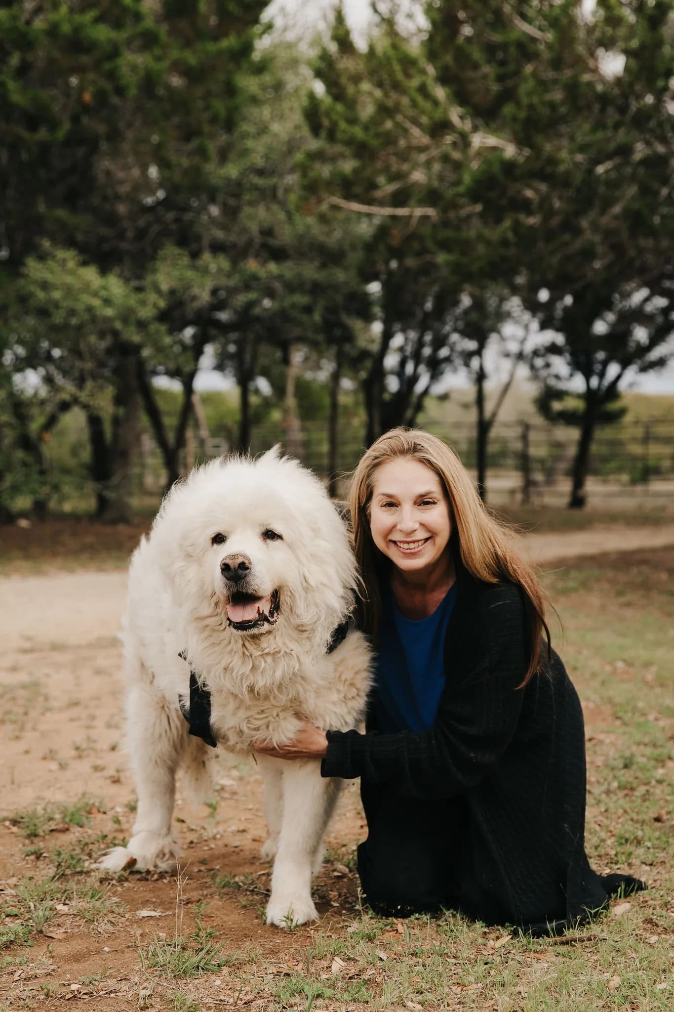 Laura kneeling beside Henry, her Great Pyrenees, on a tree-lined path